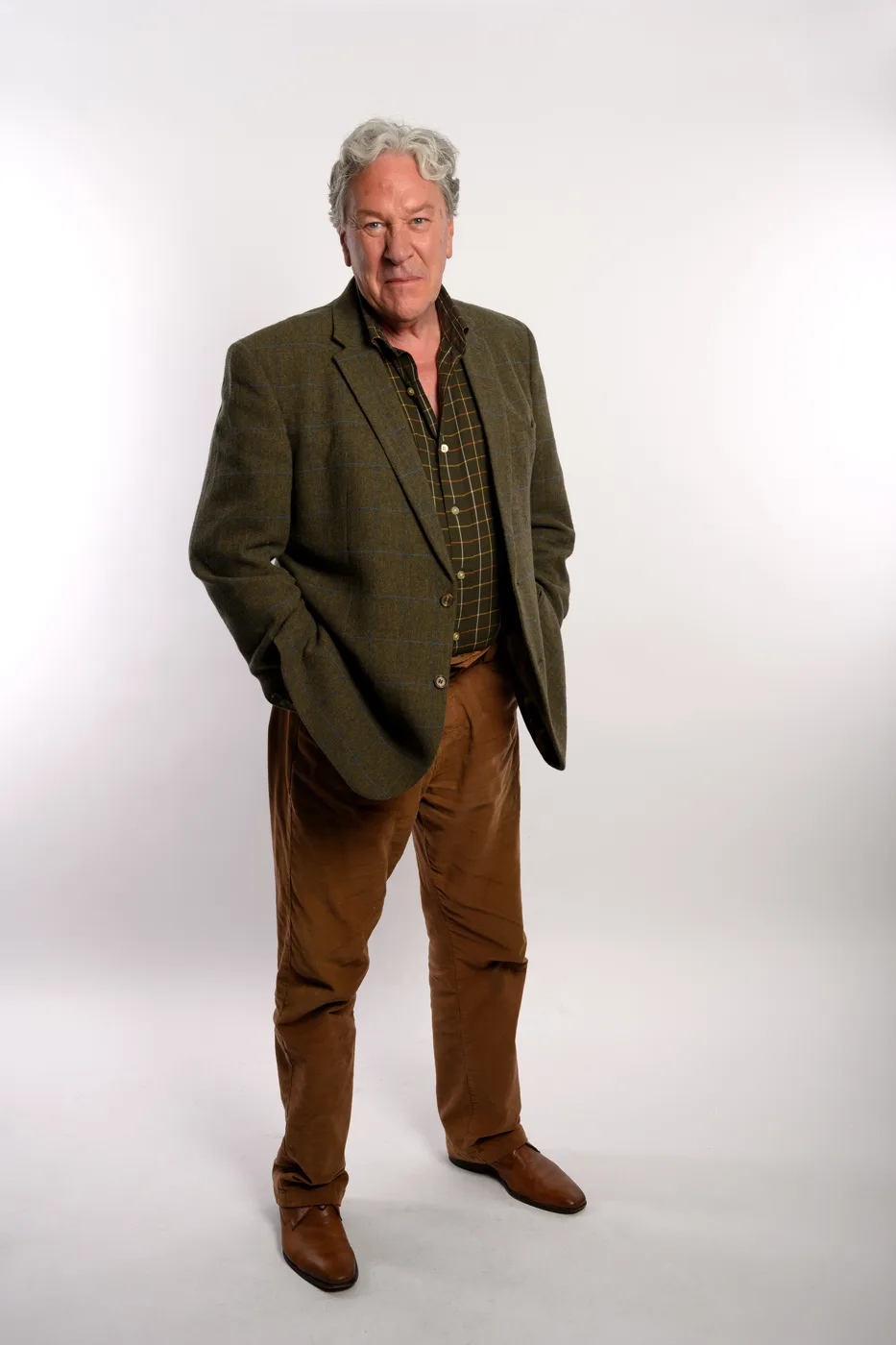 Tim Bentinck standing in a tweed jacket and brown trousers against a white studio background