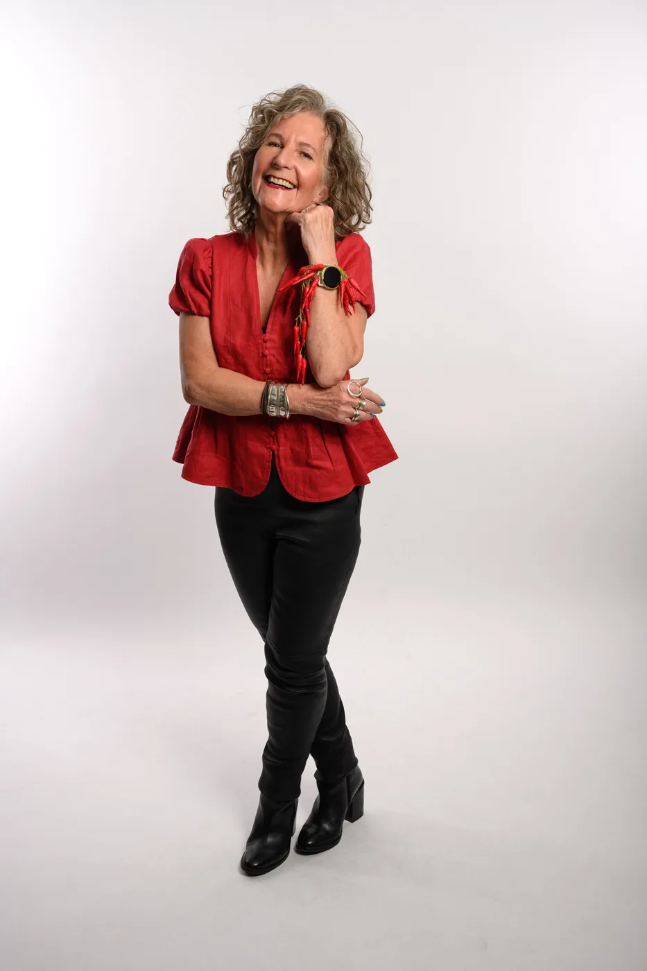 Charlotte Martin smiling in a red top and black trousers against a white studio background