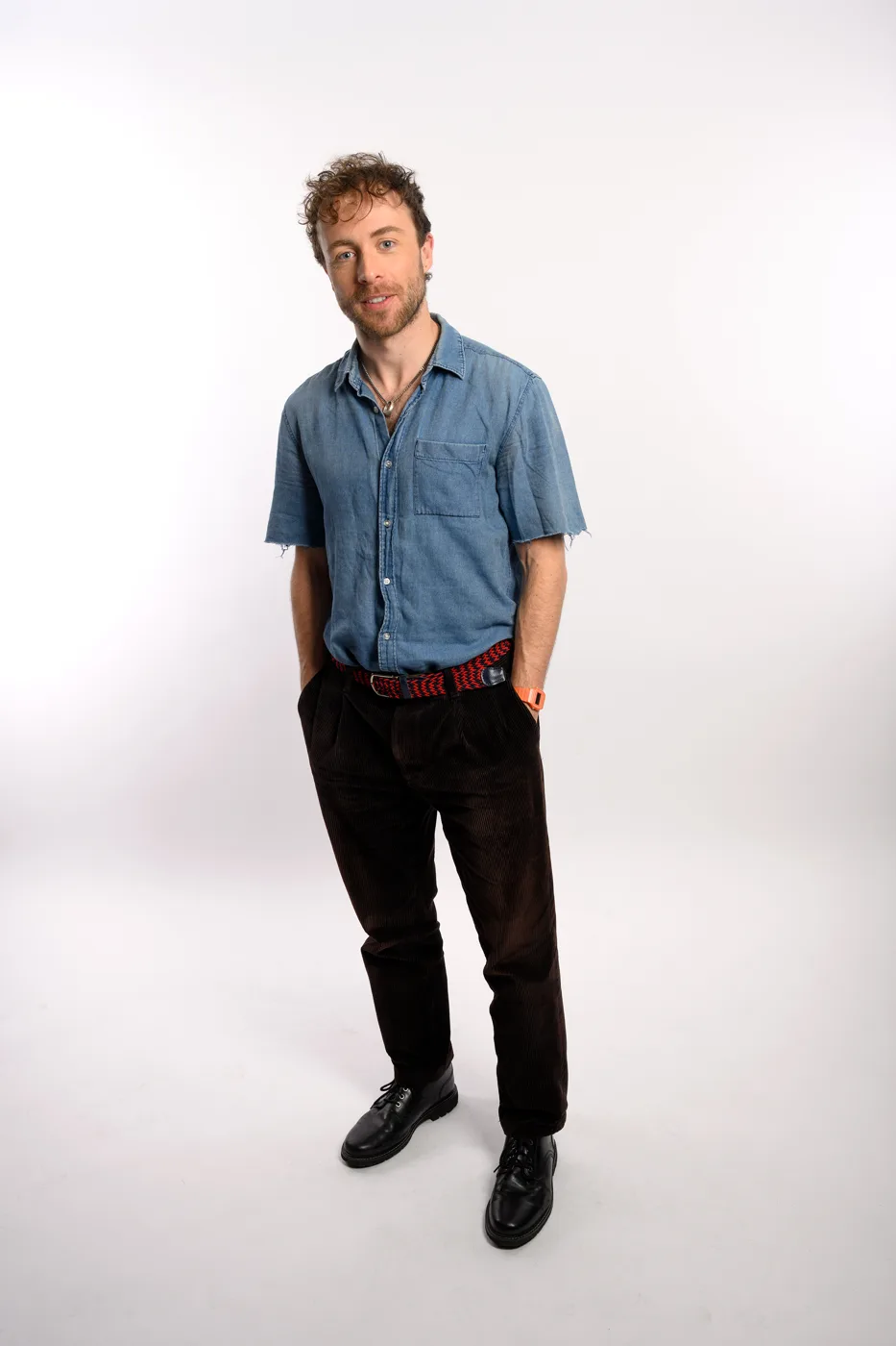 Ben Norris in a denim shirt and dark trousers against a white studio background